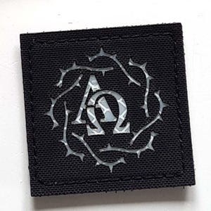 Könnte beinhalten: Zwei schwarze Stoffaufnäher. Der größere Aufnäher hat drei Löwenfiguren in Schwarz, Rot und Gelb und den Text "LASER PATCH" in Weiß. Der kleinere Aufnäher zeigt ein silbernes Design der griechischen Buchstaben Omega und Alpha, umgeben von Dornen.