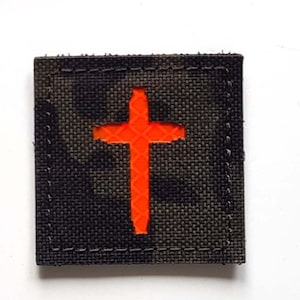 Könnte beinhalten: Zwei gestickte Aufnäher. Der obere Aufnäher ist schwarz mit einem weißen und roten Löwenmuster und dem Text "LASER PATCH". Der untere Aufnäher ist ein Tarnmuster mit einem leuchtend orangefarbenen Kreuz.