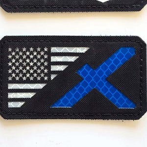 Könnte beinhalten: Zwei schwarze rechteckige Aufnäher. Der obere Aufnäher hat drei Löwenfiguren in Schwarz, Rot und Gelb und den Text "LASER PATCH" in Weiß. Der untere Aufnäher zeigt ein schwarz-weißes Design der amerikanischen Flagge und ein blaues X.