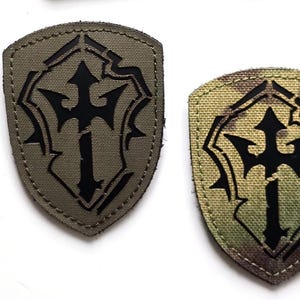 Op de afbeelding: Drie tactische patches. De bovenste patch is zwart met de tekst "LASER PATCH" en een ontwerp van drie leeuwen in rood, geel en zwart. De onderste patches zijn schildvormig met een zwart drietandontwerp op olijfgroene en camouflage achtergronden.