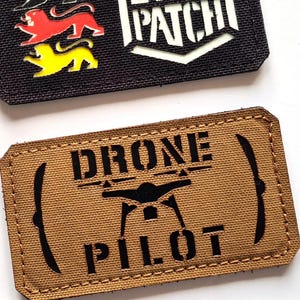 May include: Two rectangular patches. The top patch is black with the text "LASER PATCH" in white and a shield design. Below are three colored panther figures. The bottom patch is tan with the text "DRONE PILOT" and a drone graphic.
