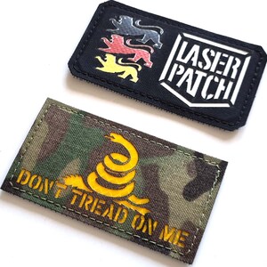 Könnte beinhalten: Zwei gestickte Aufnäher. Ein schwarzer Aufnäher zeigt drei Löwensilhouetten und den weißen Schriftzug "LASER PATCH". Der andere Aufnäher hat ein Tarnmuster mit einer gelben Schlange und dem Text "DON'T TREAD ON ME".