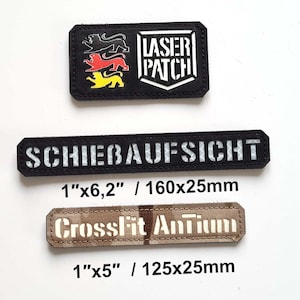 Peut inclure: Trois patchs en tissu noir, blanc et gris avec du texte blanc. Le patch du haut a un fond noir avec une bordure blanche et le texte "LASER PATCH". Le patch du milieu a un fond noir avec le texte "SCHIEBAUFSICHT". Le patch du bas a un motif camouflage avec le texte "CrossFit AnTium". Les patchs sont étiquetés avec leurs dimensions en pouces et en millimètres.