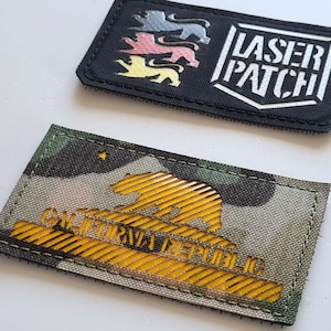 Könnte beinhalten: Zwei gestickte Patches. Der erste Patch ist schwarz mit weißem Text, der "LASER PATCH" lautet, und einem Design aus drei Löwen in verschiedenen Farben. Der zweite Patch ist Tarnmuster mit einer gelben Umrandung eines Bären und dem Text "CALIFORNIA REPUBLIC" in Gelb.