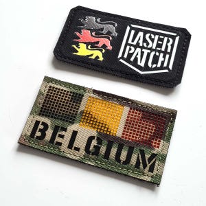 Puede incluir: Dos parches rectangulares. Un parche negro con tres leones plateados, rojos y amarillos, con el texto "LASER PATCH" en blanco. El otro parche tiene un patrón de camuflaje con la palabra "BELGIUM" en negro.