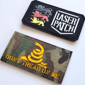 Könnte beinhalten: Zwei gestickte Aufnäher. Ein schwarzer Aufnäher zeigt drei farbige Löwen und den weißen Schriftzug "LASER PATCH". Der andere Aufnäher hat ein Tarnmuster mit einer gelben Schlange und dem Text "DON'T TREAD ON ME".