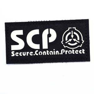 May include: Black rectangular patch with white text and a symbol. The text reads "SCP Secure. Contain. Protect." The symbol is a circle with three arrows pointing inward. The patch is likely made of fabric.
