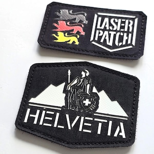 Könnte beinhalten: Zwei schwarze, gestickte Aufnäher. Einer zeigt drei Löwen in Grau, Rot und Gelb sowie den weißen Text "LASER PATCH". Der andere Aufnäher zeigt eine weiße Bergkette, eine Figur, einen Schild mit Kreuz und das Wort "HELVETIA" in Weiß.