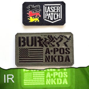 Könnte beinhalten: Zwei rechteckige Aufnäher. Der obere Aufnäher ist schwarz mit einem weißen Logo und dem Text "LASER PATCH". Der untere Aufnäher ist olivgrün mit dem Text "BUR", "A+POS", "NKDA" und einer amerikanischen Flagge.