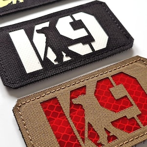 Könnte beinhalten: Zwei schwarze und braune Patches mit den Buchstaben "K9" und einer Silhouette eines Hundes in weißem und rotem reflektierendem Material.