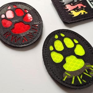 May include: Two black fabric patches with a paw print design. The paw print on the left patch is red and the paw print on the right patch is yellow.