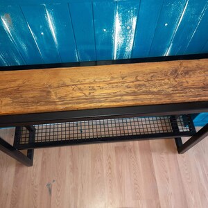 May include: A black metal console table with a wood top and a wire shelf. The table is against a blue wall.