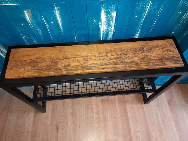 May include: A black metal console table with a wood top and a wire shelf. The table is against a blue wall.