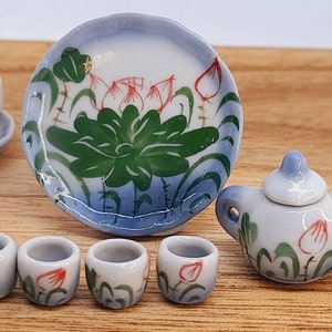 Peut inclure: Petit service à thé en porcelaine avec un motif floral bleu et blanc. L'ensemble comprend une théière, une soucoupe, une assiette et de petites tasses. L'assiette présente un motif de fleur de lotus avec des feuilles vertes et des accents rouges.