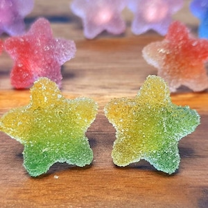 Puede incluir: Primer plano de caramelos en forma de estrella con una capa de az&uacute;car. Los caramelos son de varios colores, incluyendo amarillo, verde, rojo y morado. Los caramelos est&aacute;n sobre una superficie de madera. Un dulce.