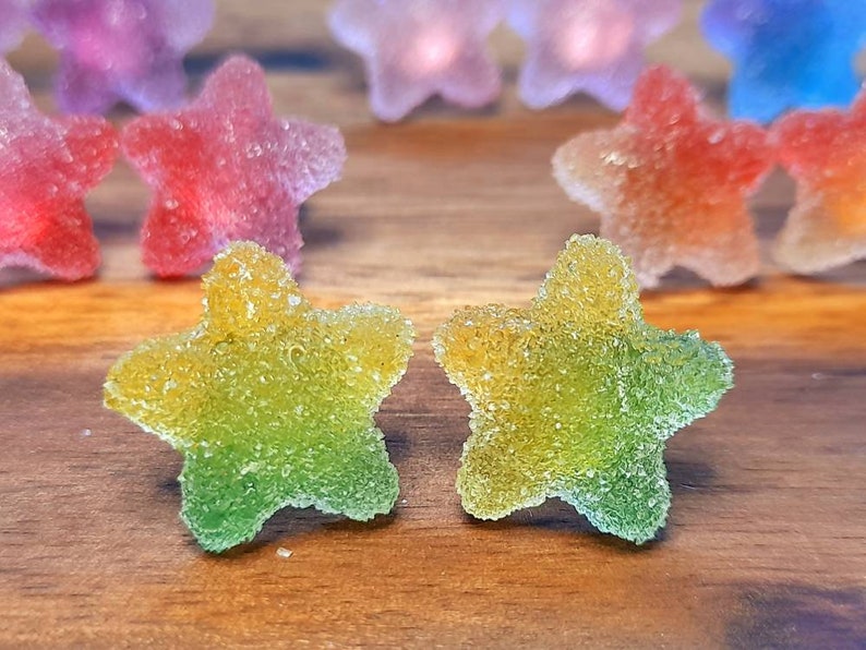 Puede incluir: Primer plano de caramelos en forma de estrella con una capa de az&uacute;car. Los caramelos son de varios colores, incluyendo amarillo, verde, rojo y morado. Los caramelos est&aacute;n sobre una superficie de madera. Un dulce.