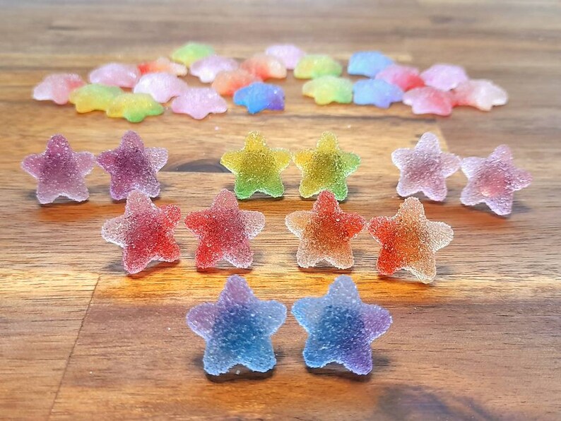 Puede incluir: Un surtido de caramelos coloridos en forma de estrella con una capa de az&uacute;car. Los caramelos son en tonos de rojo, naranja, amarillo, verde, morado y azul. Algunos est&aacute;n dispuestos en pares, otros est&aacute;n dispersos.