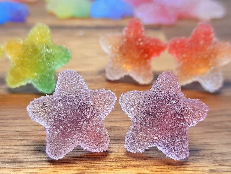Puede incluir: Primer plano de caramelos coloridos en forma de estrella con una capa de az&uacute;car. Los caramelos son de color p&uacute;rpura, rojo, naranja, amarillo y verde. Los caramelos est&aacute;n sobre una superficie de madera.