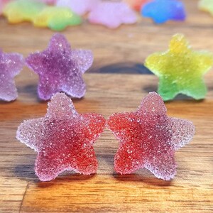 Puede incluir: Primer plano de caramelos con forma de estrella coloridos con una capa de az&uacute;car. Los caramelos son de color rojo, morado, amarillo y verde, dispuestos sobre una superficie de madera. Los caramelos tienen un aspecto transl&uacute;cido.
