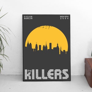 May include: A black and white poster with a yellow sun and a cityscape silhouette. The text "the KILLERS" is in white with a pixelated effect. The text "C-CLUB BERLIN" and "NOV 6TH 2004" are in white.