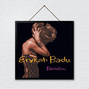 May include: A framed print featuring a sepia-toned image of Erykah Badu. The artwork shows a person with their head in their hands, wearing a patterned dress. The words "Erykah Badu" and "Baduizm" are written on the image.