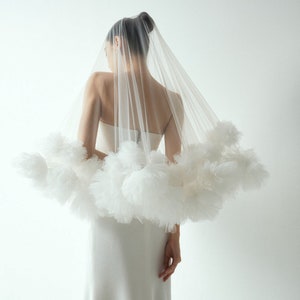 Puede incluir: Un velo de tul blanco con un gran diseño circular y esponjoso. El velo lo lleva una persona de espaldas a la cámara.