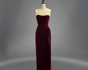 Könnte beinhalten: Ein trägerloses, burgunderfarbenes Samtkleid mit einem hohen Schlitz. Das Kleid hat ein figurbetontes Oberteil und einen fließenden Rock.