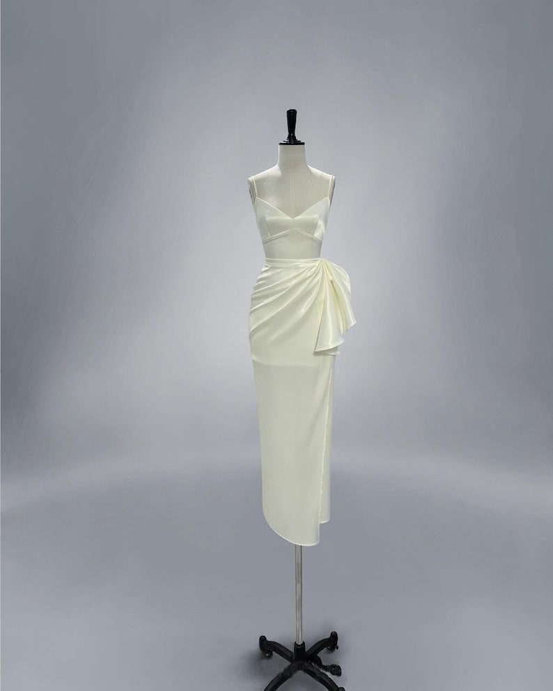 May include: A white satin dress with a fitted bodice and a flowing skirt. The skirt has a large bow on the side.