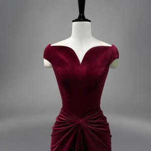 May include: A burgundy velvet dress with a sweetheart neckline and a fitted bodice. The dress has a gathered skirt and short cap sleeves.