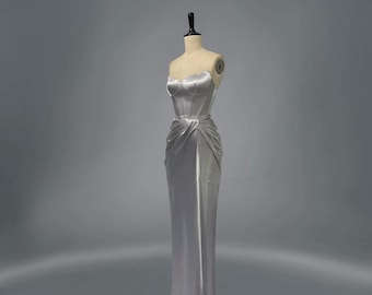 Könnte beinhalten: Ein silbernes Satin-Kleid ohne Träger mit einem figurbetonten Oberteil und einem fließenden Rock.