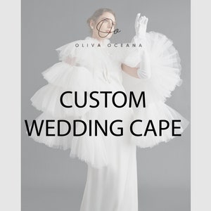 Pode incluir: Uma capa de casamento de tule branco com um design de babados. A capa é usada por uma modelo e o texto "CUSTOM WEDDING CAPE" é exibido abaixo da modelo.