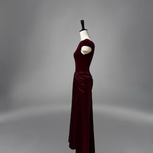 May include: A burgundy velvet dress with a fitted bodice and a flowing skirt. The dress has a scoop neckline and short sleeves.