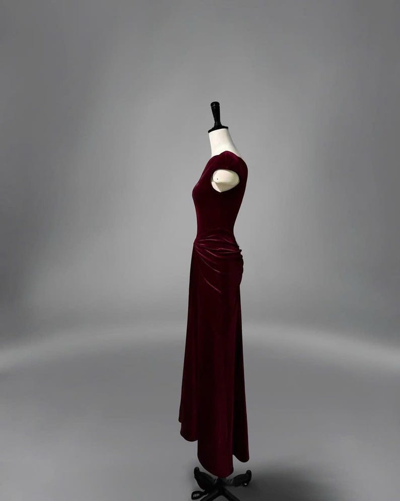 May include: A burgundy velvet dress with a fitted bodice and a flowing skirt. The dress has a scoop neckline and short sleeves.
