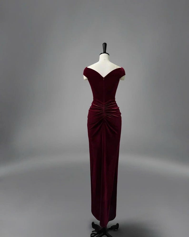 May include: A long, burgundy velvet dress with a V-neckline and short sleeves. The dress has a fitted bodice and a flowing skirt.