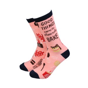 May include: Pink socks with a navy blue cuff and a pattern of various baked goods and the text "Good things come to those who bake."