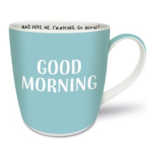 Op de afbeelding: Een lichtblauwe keramische mok met een wit handvat. De mok heeft de woorden "GOOD MORNING" in grote witte letters op de voorkant. De rand van de mok heeft de tekst "AND HERE WE F***ING GO AGAIN!"