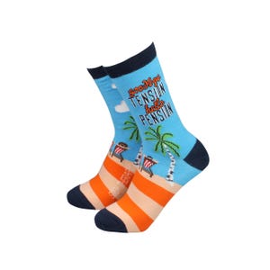 May include: Novelty socks featuring a beach scene with palm trees and deckchairs. The socks are light blue with the words "Goodbye Tension Hello Pension". The socks have orange and white stripes and navy blue accents.