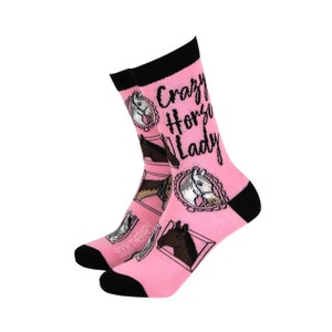 May include: Pink socks with a black trim and a white horse design. The socks have the text "Crazy Horse Lady" printed on them.