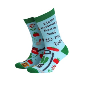 Könnte beinhalten: Ein Paar blaue Socken mit grünem Bündchen. Die Socken haben ein Gartenthema mit Illustrationen von Tomaten, Blumen, einer Gießkanne und einer Schaufel. Der Text auf den Socken lautet "Ich liebe Gärtnern von Kopf bis Fuß".