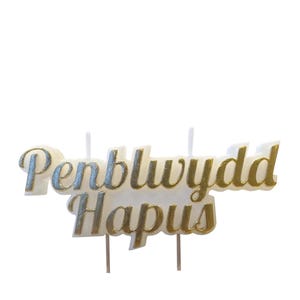Puede incluir: Topper de pastel dorado con las palabras "Penblwydd Hapus" que significa "Feliz cumpleaños" en galés.