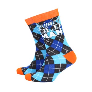 Puede incluir: Un par de calcetines de color azul y negro con estampado de rombos y puño naranja. Los calcetines tienen el texto "GRUMPY OLD MAN" impreso en blanco.