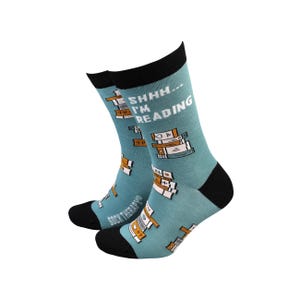 May include: A pair of blue socks with a black cuff. The socks feature a stack of books with the text "Shhh... I'm reading" on the front.