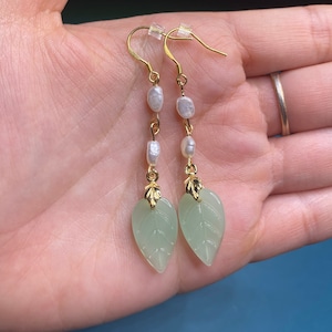 May include: A pair of gold earrings with green leaf-shaped pendants and white pearl accents.