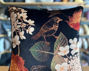 May include: A black velvet pillow with a floral and bird design. The flowers are white and pink with gold accents. The bird is brown with gold accents. The pillow is perfect for adding a touch of elegance to any room.