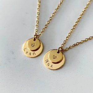 May include: Two gold necklaces with small round pendants. The pendants are engraved with the names "Evan" and "Mak" and a small heart symbol.