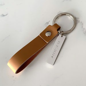 Peut inclure: Un porte-clés en cuir marron avec une étiquette en métal argentée qui dit "02.01.2020".