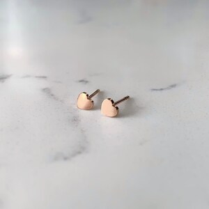 May include: A pair of small, rose gold heart-shaped stud earrings.