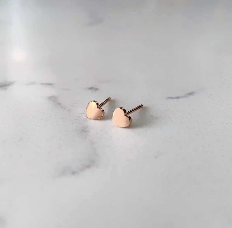 May include: A pair of small, rose gold heart-shaped stud earrings.