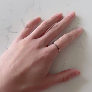 May include: A simple, thin, silver band ring worn on a finger.