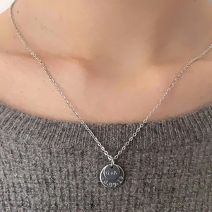 May include: A silver chain necklace with a round pendant that has the initials "G & K" and the date "18.09.14" engraved on it.